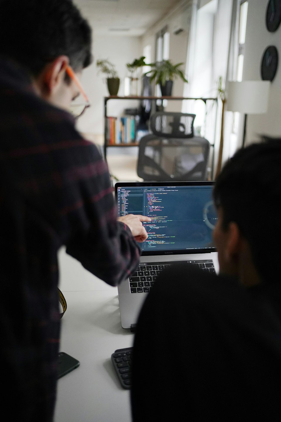 Two colleagues collaborate over code on a laptop.